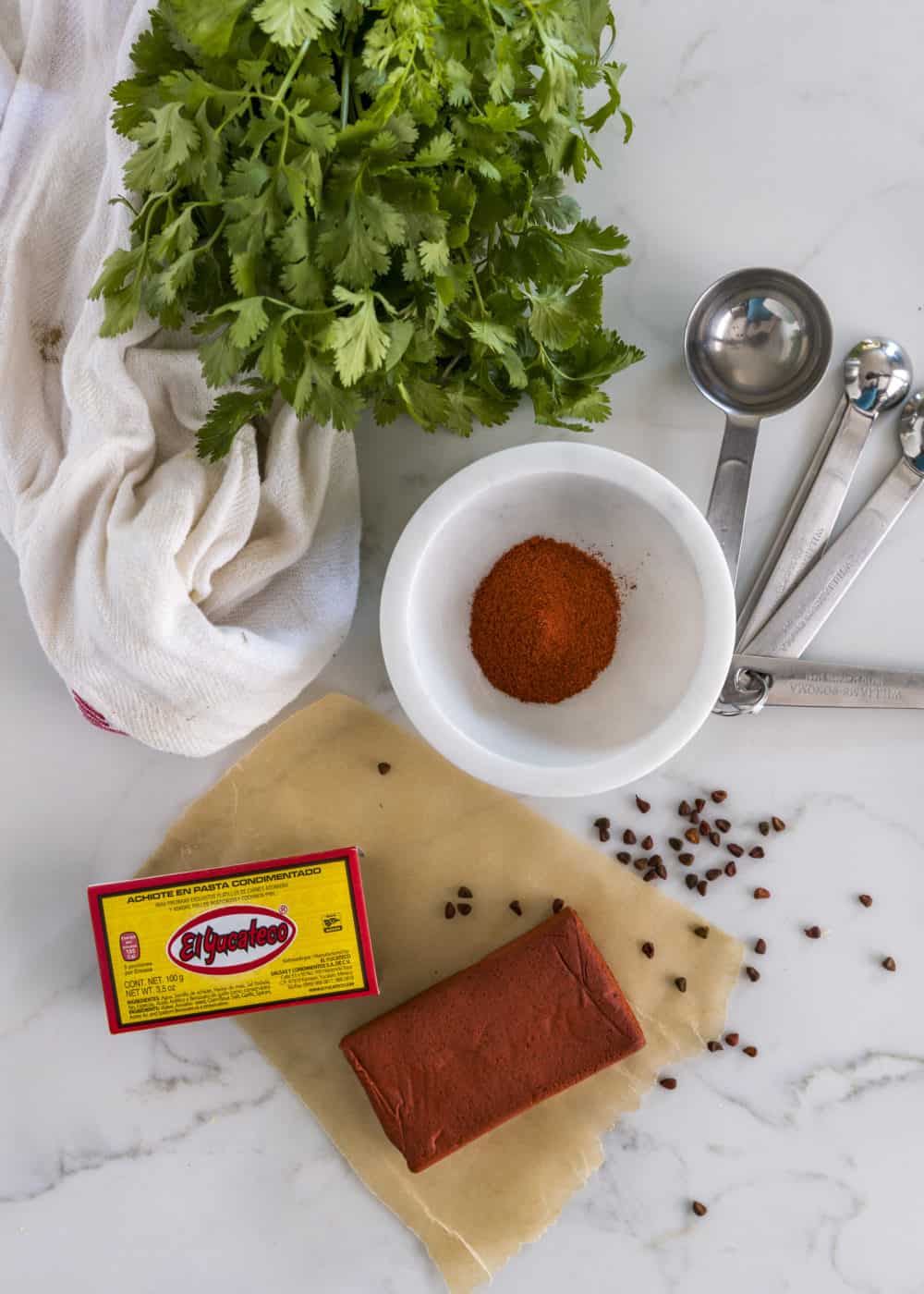 overhead image: block of achiote paste on counter with small bowl of achiote powder and bunch of cilantro