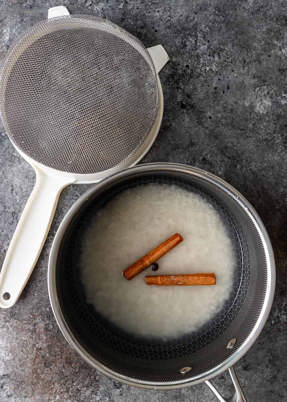 overhead: making the rice in a small saucepan with cinnamon sticks. There is a small strainer visible