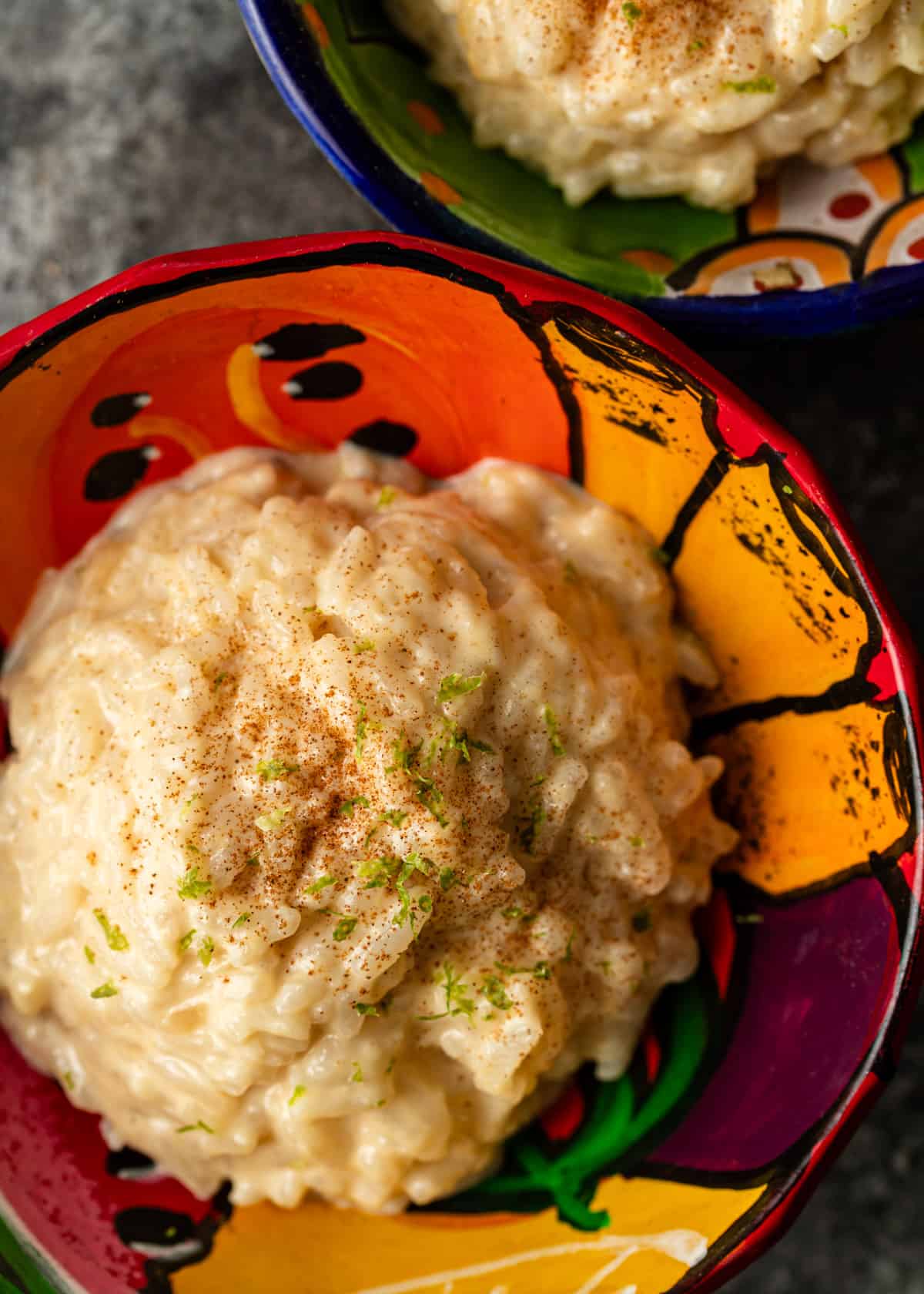 overhead closeup: arroz con leche recipe in a colorful ceramic bowl with allspice and lime zest on top