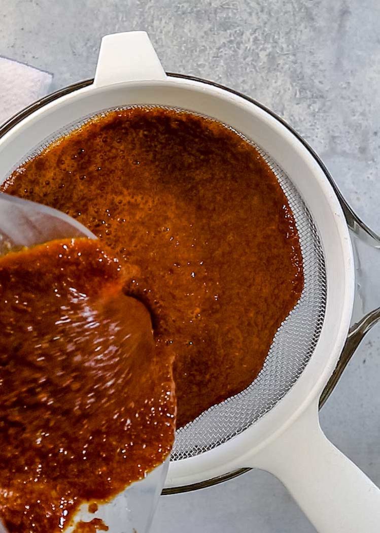 pouring mexican enchilada sauce through fine mesh sieve