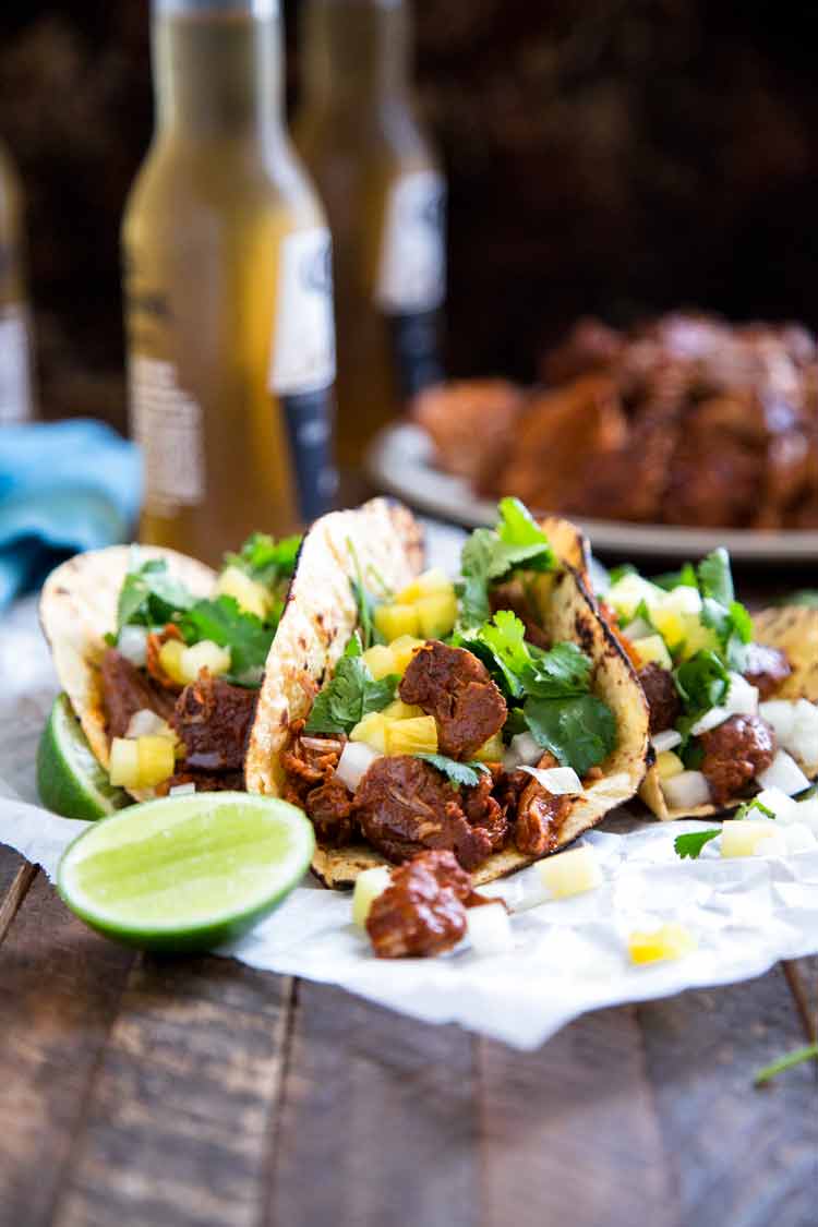 oven roasted Mexican pork tacos on a wooden table top with 2 bottles of beer in background.