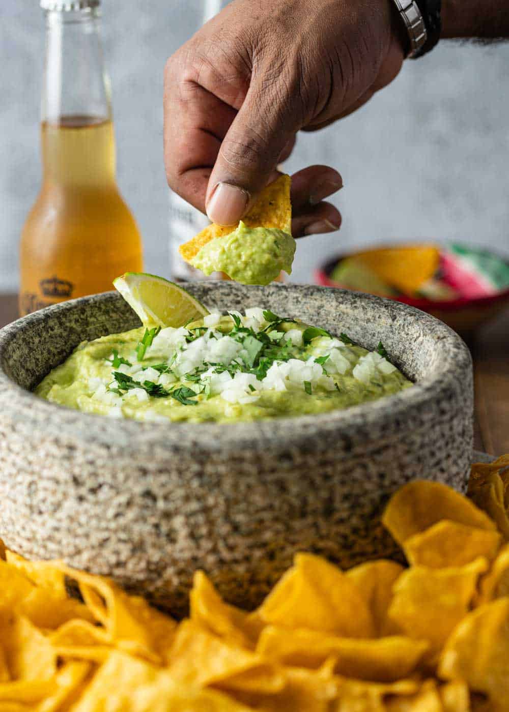 man's hand dipping tortilla chip into bowl of avocado dip