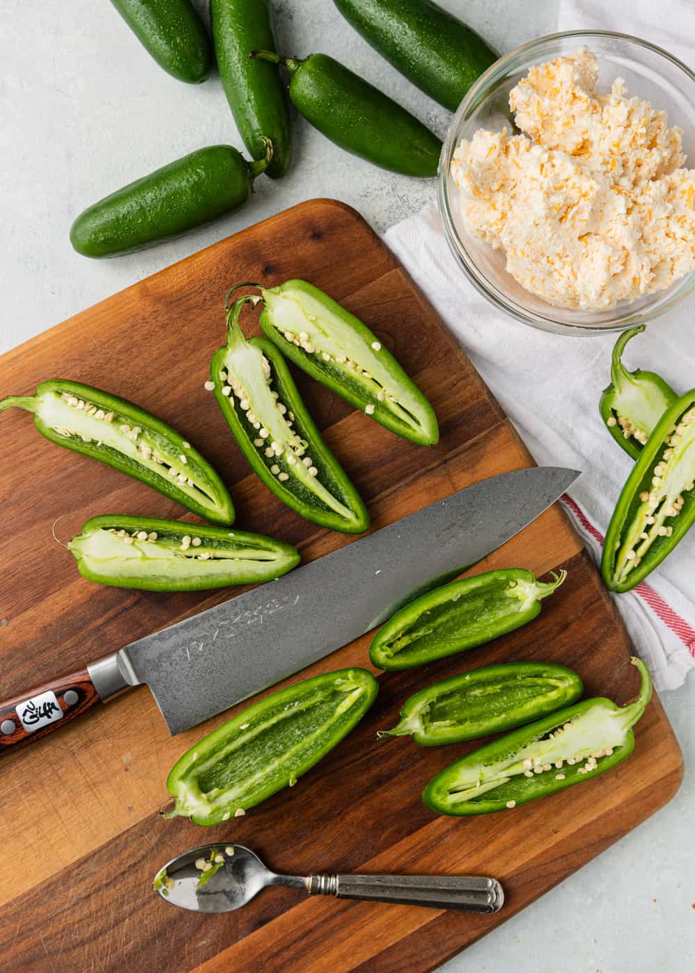 overhead; jalapenos cut in half on wood cutting board with large chef's knife