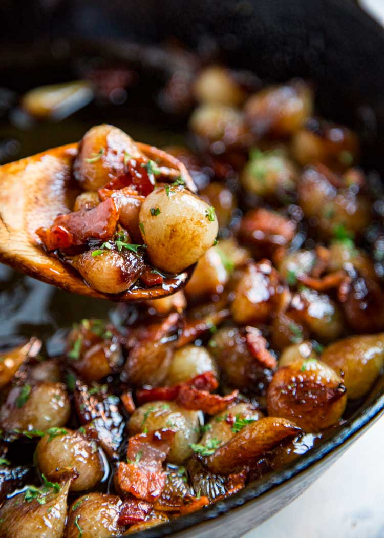 closeup: a wooden spoon lifiting pearl onions over a skillet filled with more