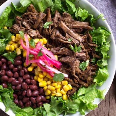 overhead: burrito bowl with shredded meat, red onion, corn and black beans on lettuce