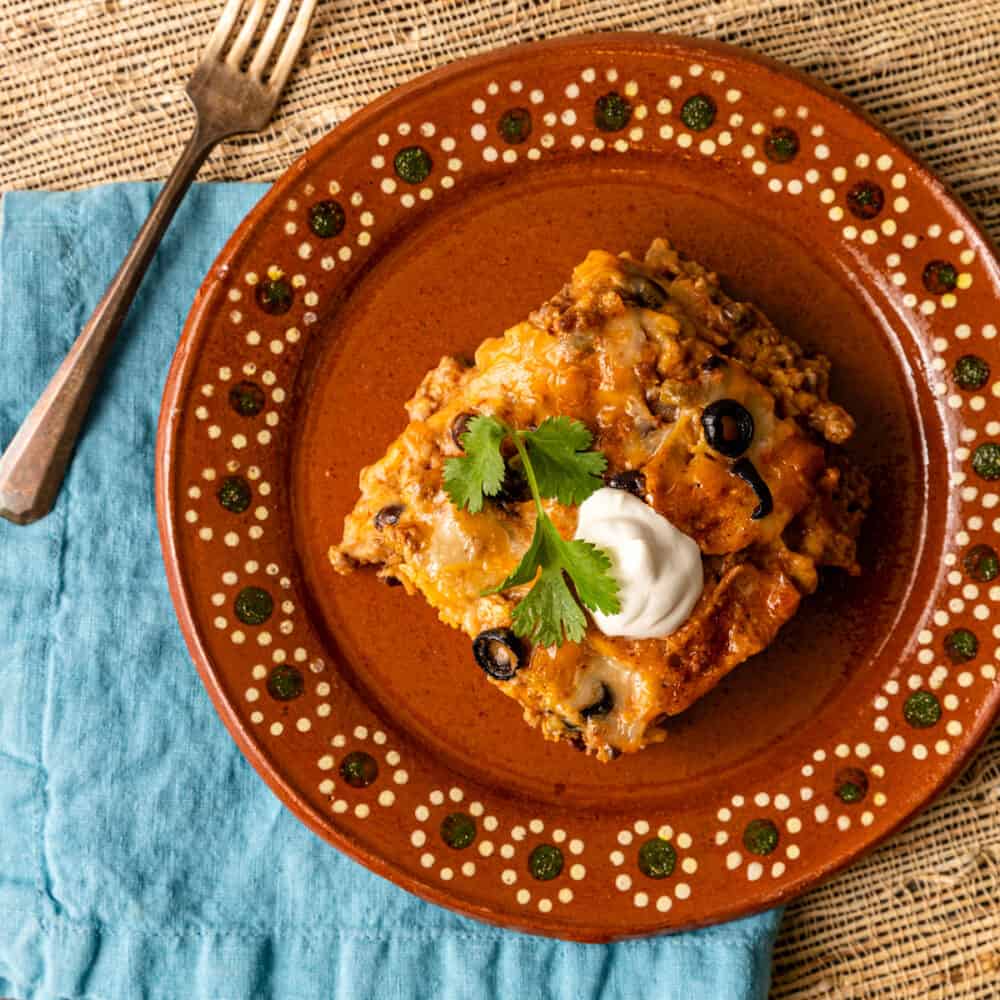 overhead: slice of beef enchilada casserole with sour cream garnish on plate