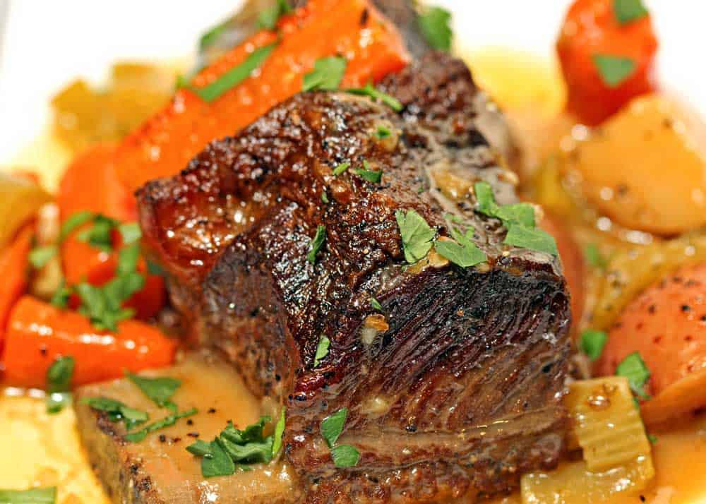 close up of braised beef short ribs, carrots and potatoes on a white dish