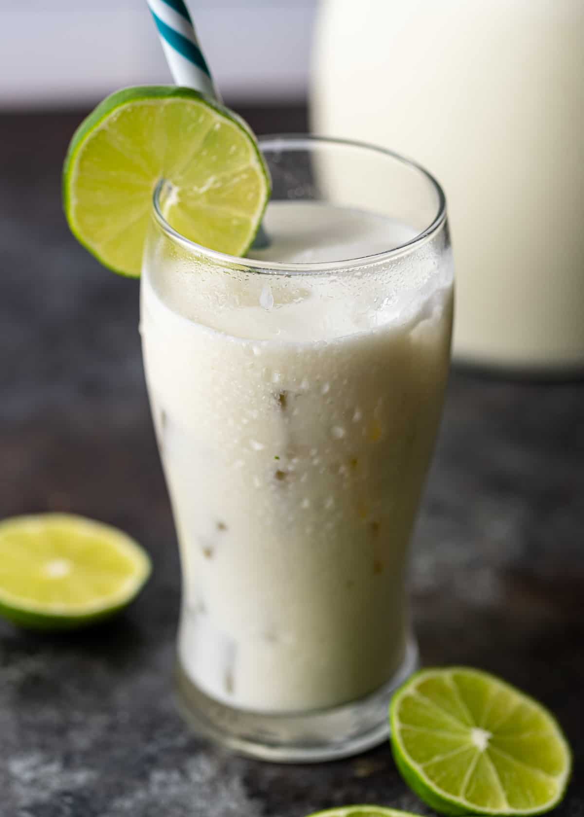 a tall glass of limonada with a lime round and a blue and white straw