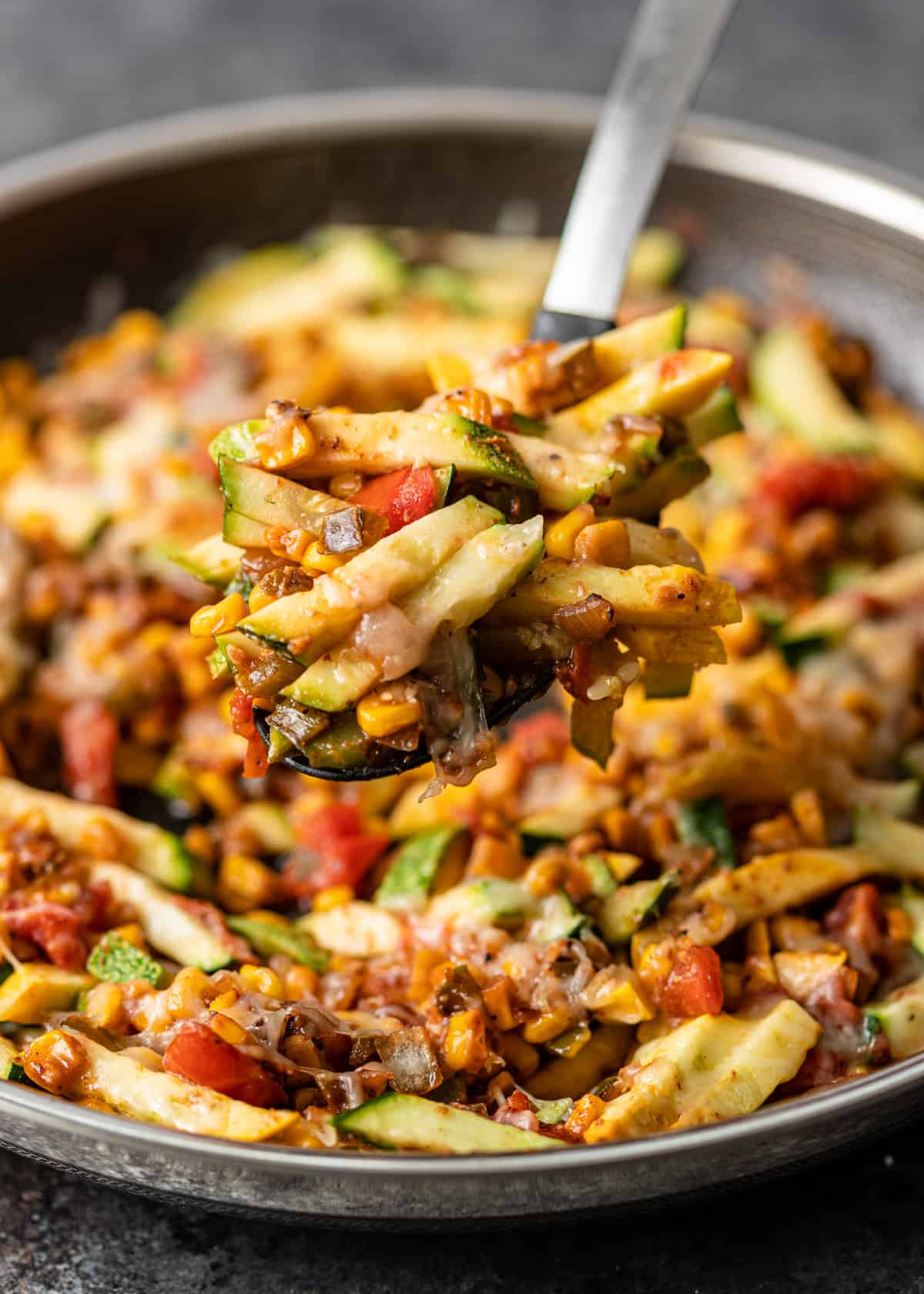 closeup: lifting calabacitas in a spoon over a large skillet with more Mexican zucchini