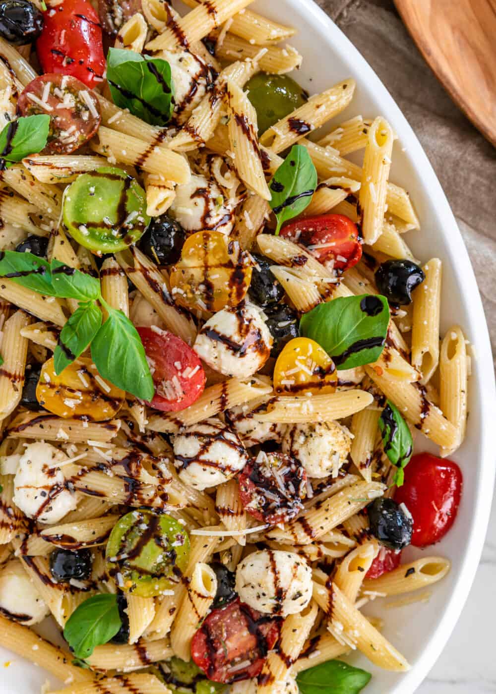 Caprese Pasta Salad on a white platter wit balsamic glaze