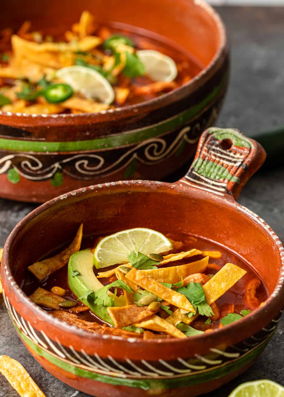 bowl with Chicken Tortilla Soup topped with cilantro, lime wedges, avocado and tortilla strips