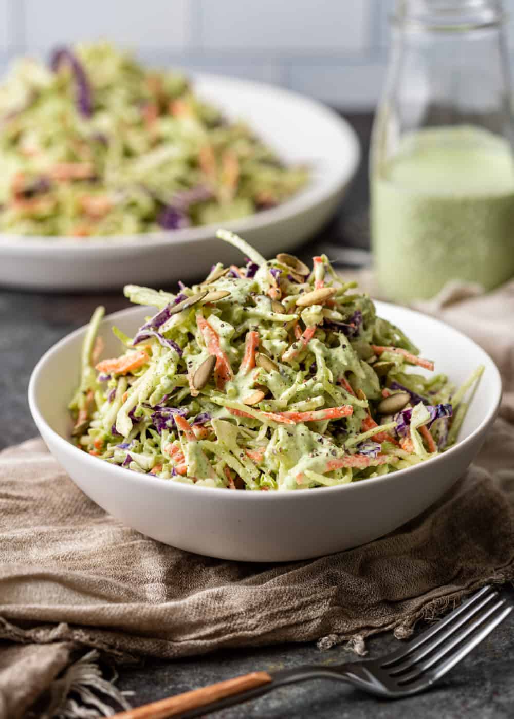 white bowl of cilantro lime coleslaw on table with bottle of homemade coleslaw dressing in background