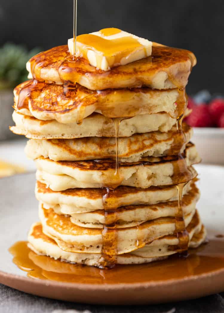 pouring syrup over stack of 10 fluffy pancakes