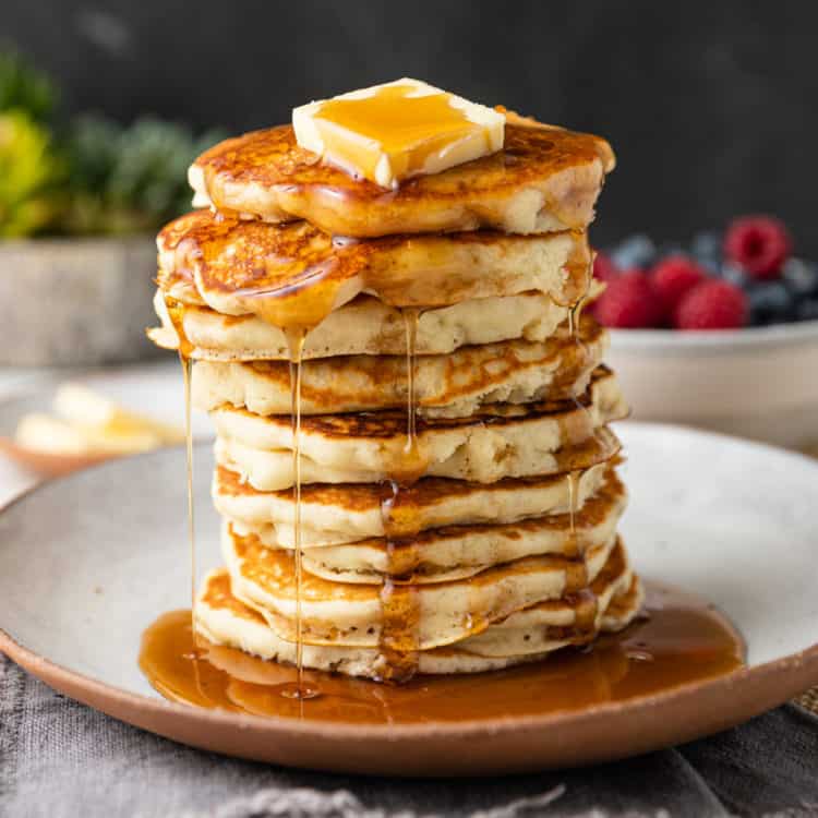 stack of fluffy golden griddle cakes with butter dripping in maple syrup