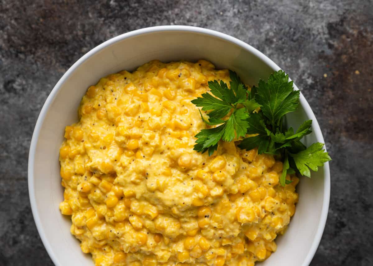 overhead: creamed corn recipe in a white bowl with fresh parsley on top