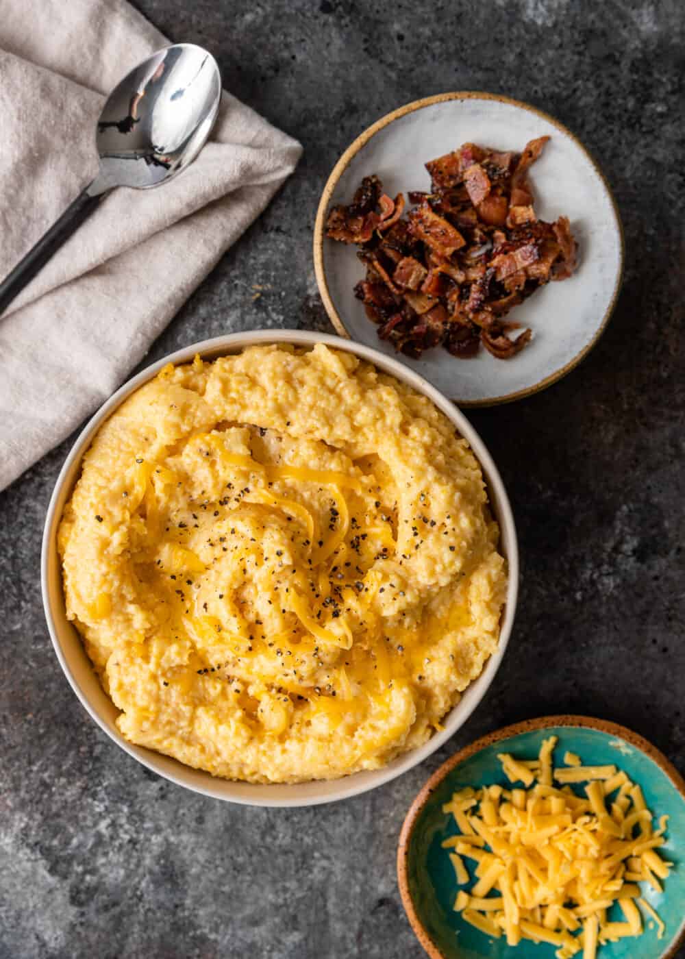 overhead: bowl of creamy grits with crumbled bacon and shredded cheese