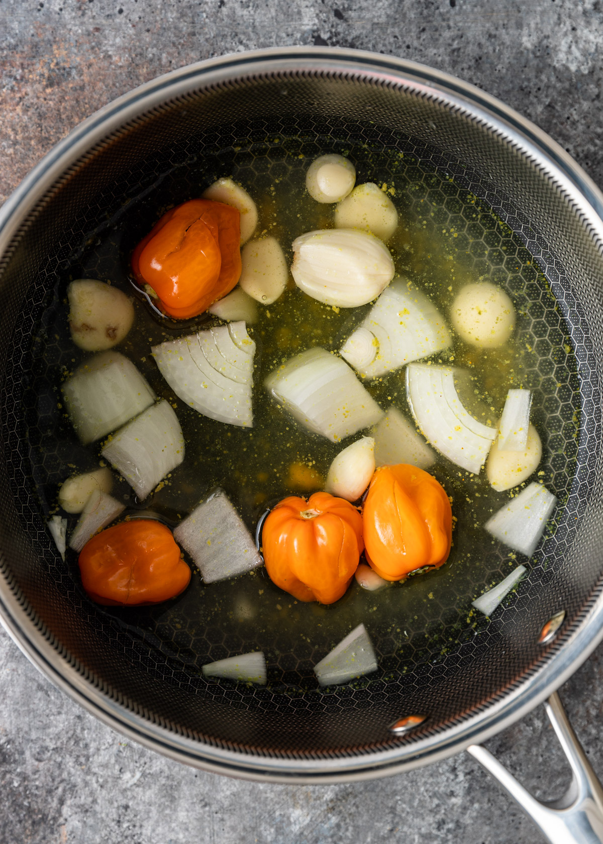 overhead: boiling onions, garlic, and peppers in a pan for habanero sauce