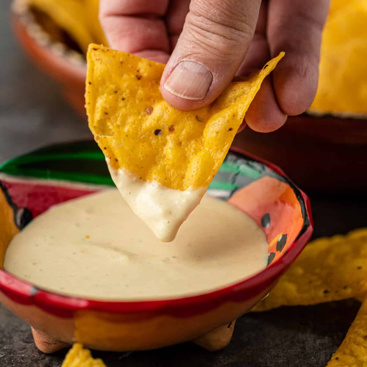 closeup: a hand dipping a tortilla chip into a small ceramic bowl of creamy habanero sauce