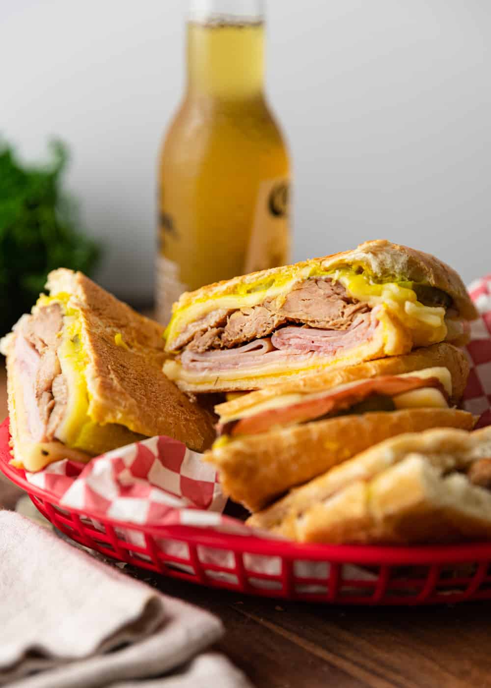 Sliced Cuban sandwiches in a basket with beer in the background.