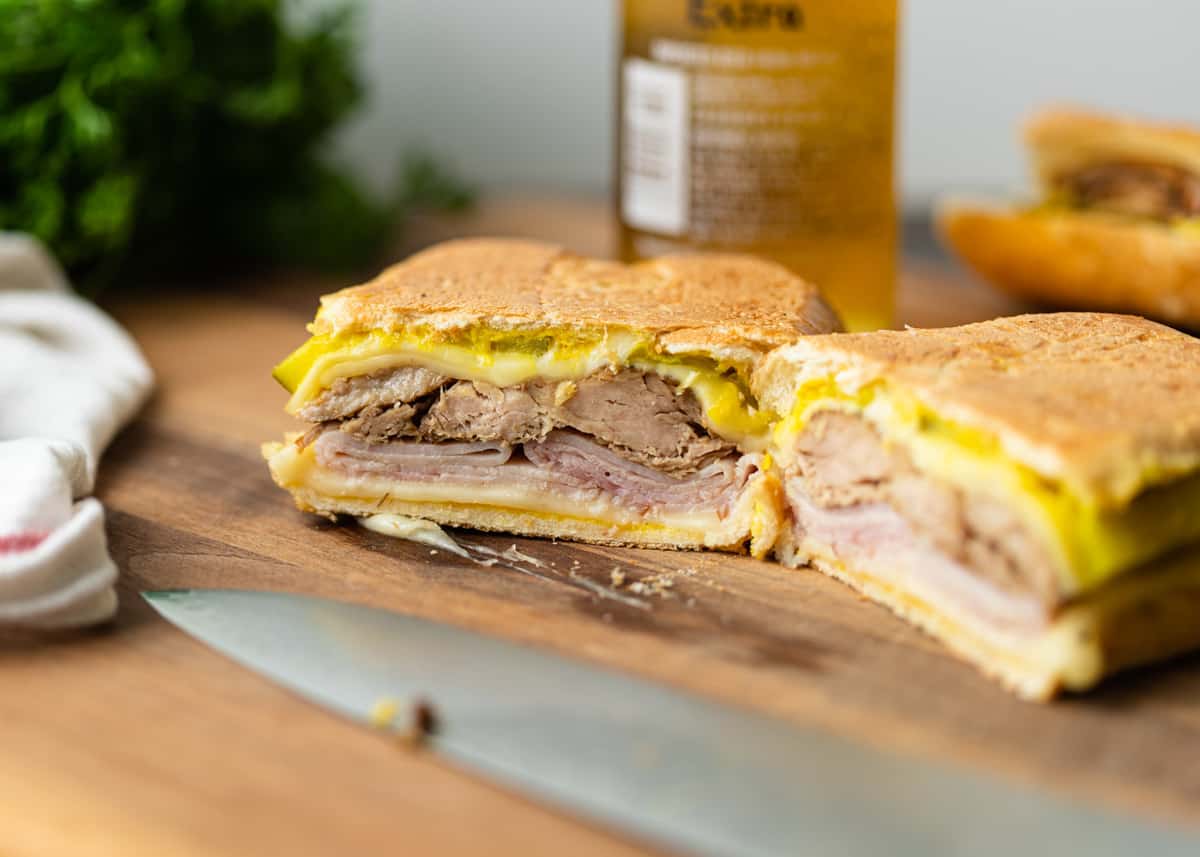 Visible layers in Cuban sandwich on a wooden cutting board, with a knife visible.