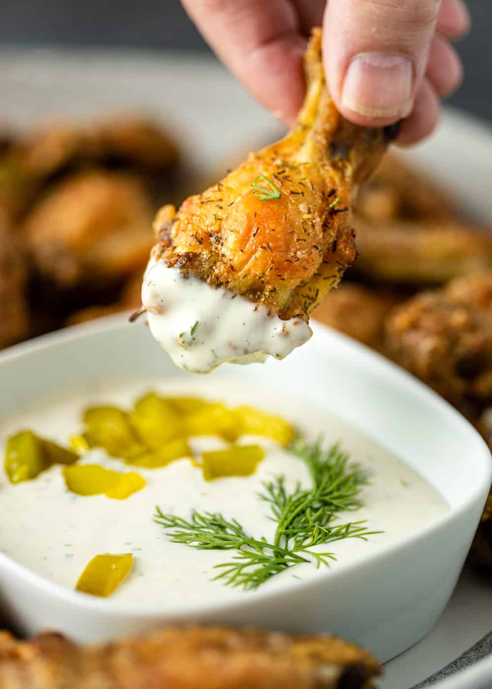 man's hand dipping crispy chicken drumette into dill dipping sauce