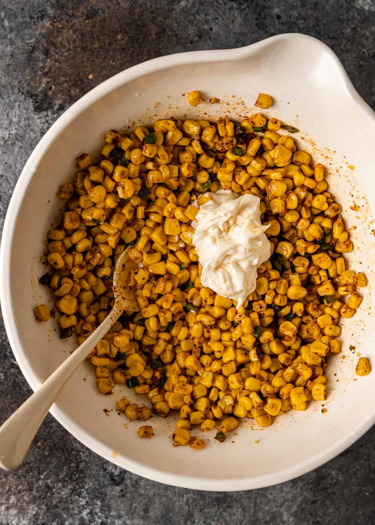 overhead: adding mayonnaise to a bowl of roasted and seasoned corn