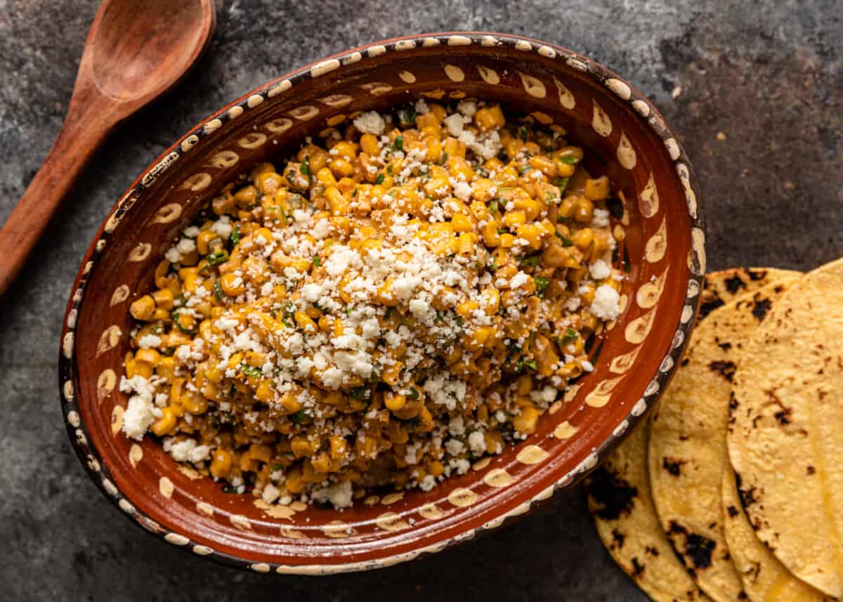 overhead: a large ceramic bowl with esquites corn salad and corn tortillas on the side