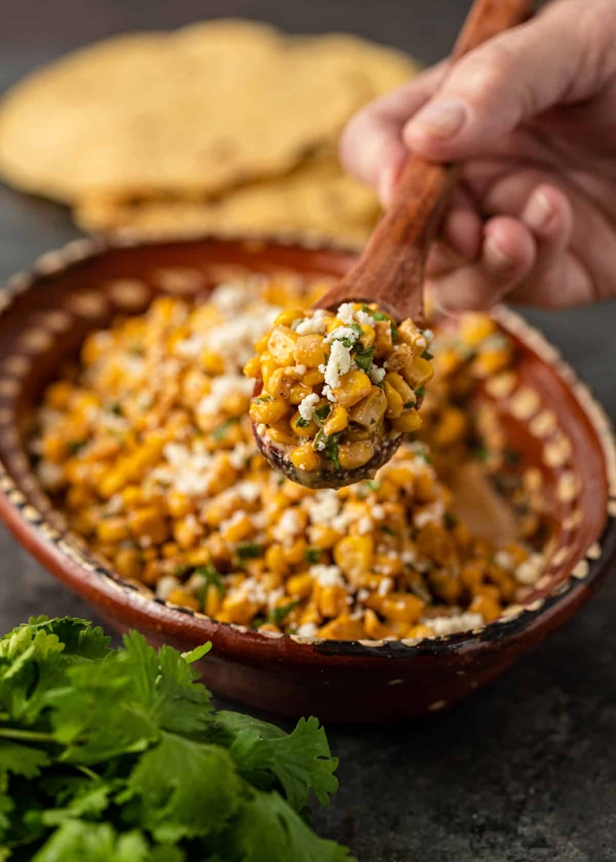 holding a spoonful of esquites over a bowl full of the corn salad