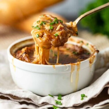 lifting spoonful of classic French onion soup out of a white bowl