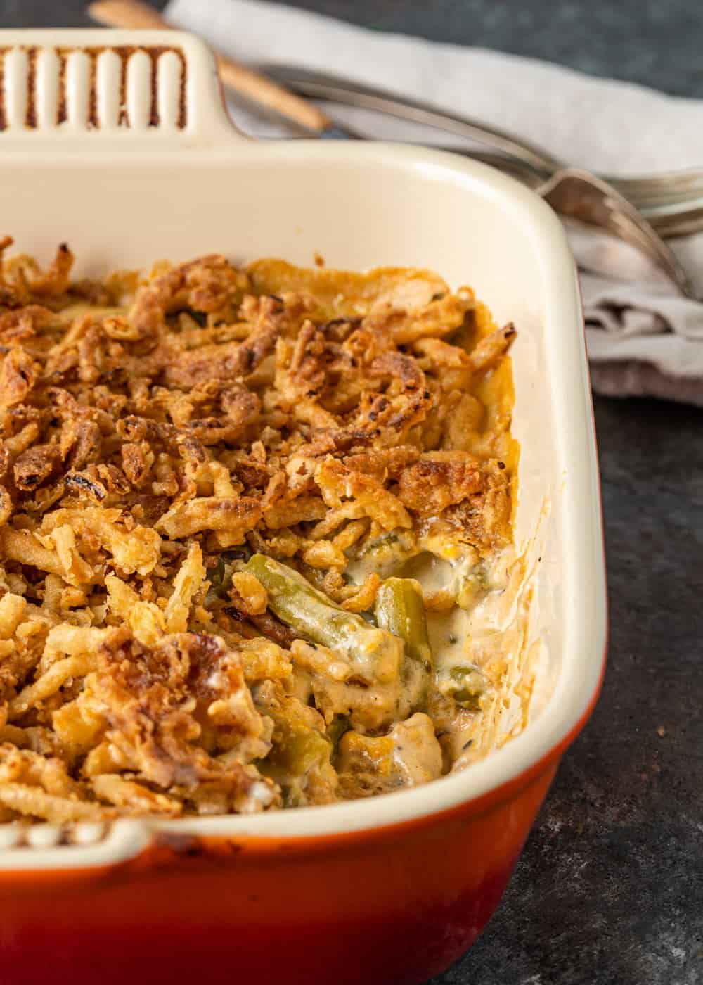 side view closeup: fried onions on top of green bean casserole in red baking dish
