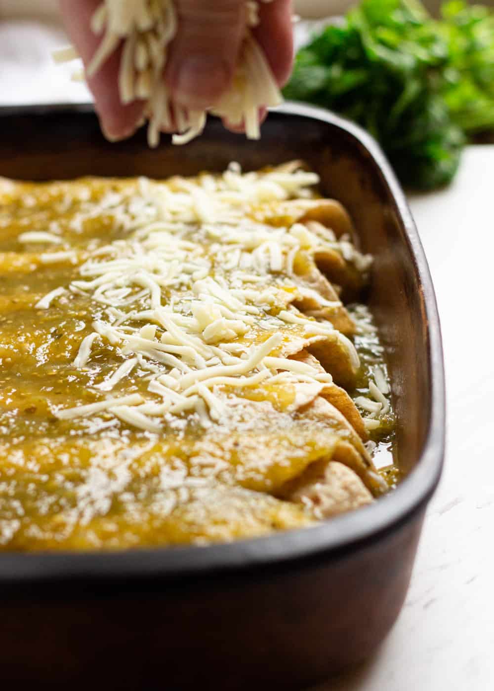 sprinkling Mexican cheese onto enchiladas in casserole dish