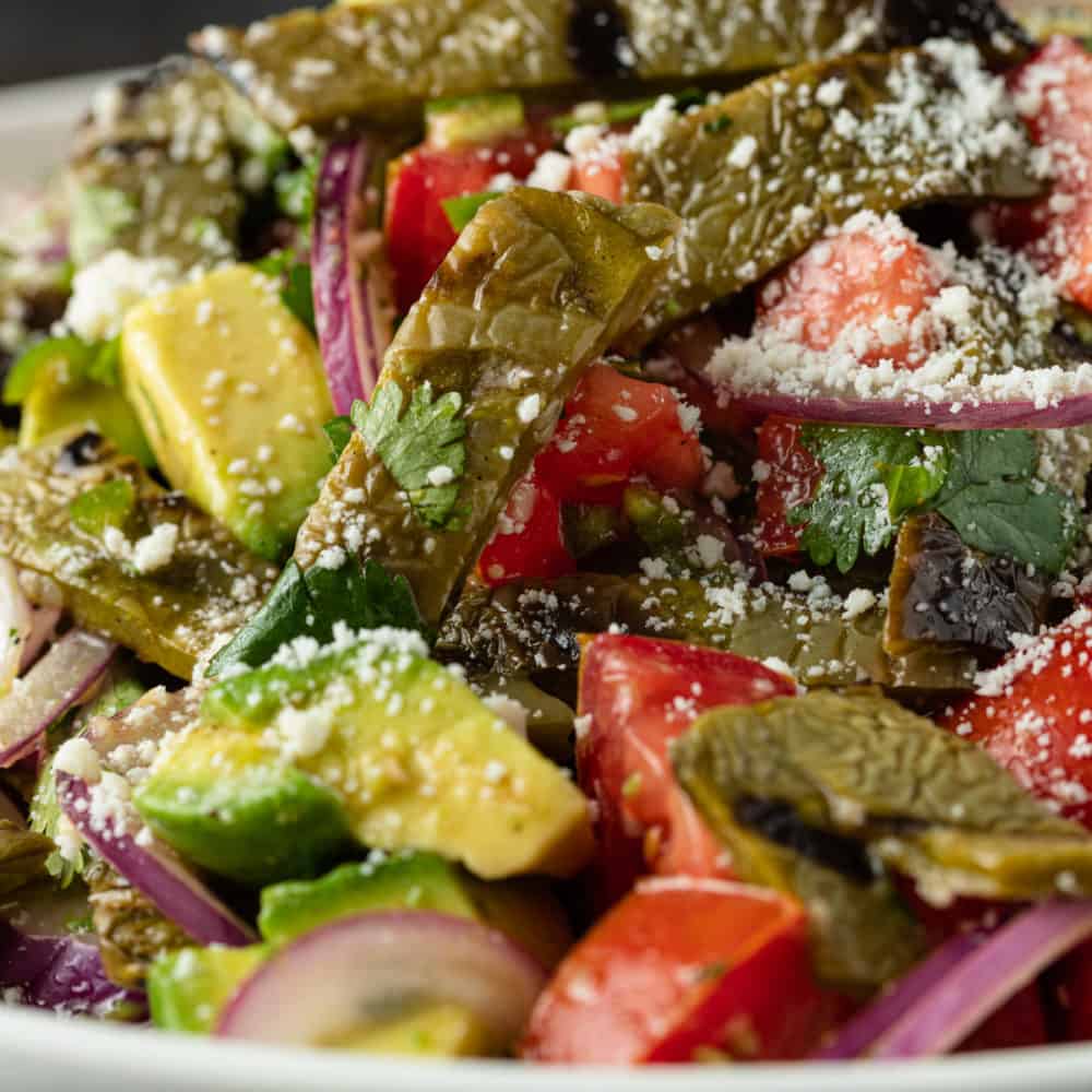 close up image of chopped avocado, tomatoes, red onion, and cactus paddles with crumbled Cojita on top