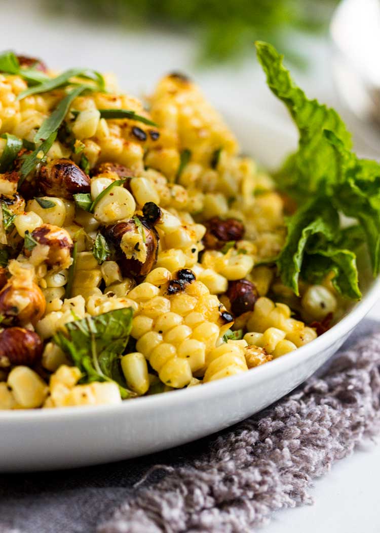 close up: grilled corn salad with hazelnuts with fresh herbs in a white bowl