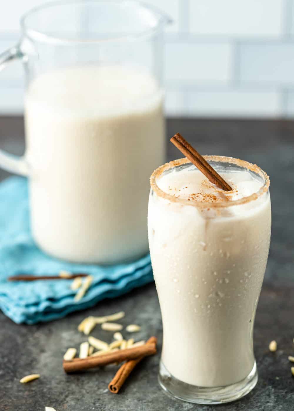 tall glass of Horchata (rice and almond milk drink) with pitcher of it in background