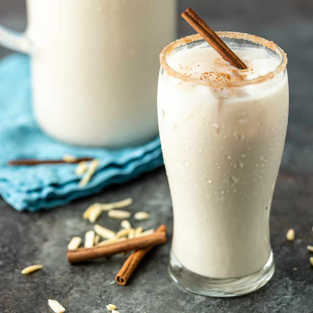 orxata (Spanish milk drink) and stick of cinnamon in tall glass rimmed with cinnamon sugar