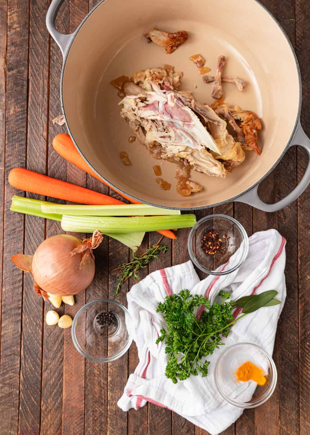 large pot with chicken carcass next to carrots, celery, onion, and herbs