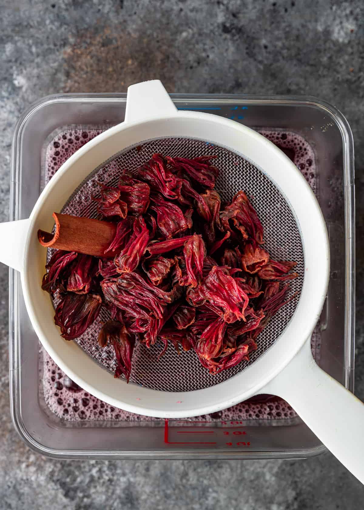 overhead: straining cooked hibiscus flowers over a blender