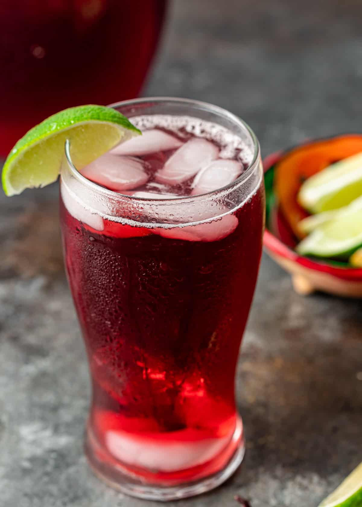 closeup: a tall glass of agua de jamaica with ice and a lime slice as a garnish