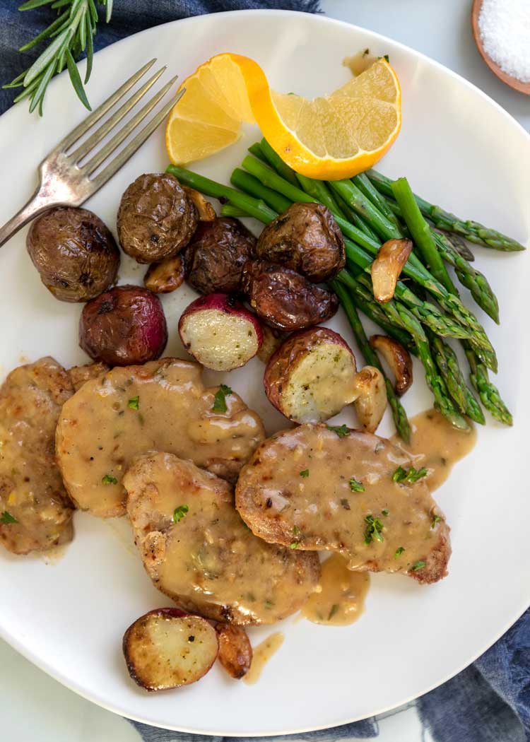 overhead plate of Lemon, Rosemary Pork Medallions served on white plate with potatoes and asparagus. 