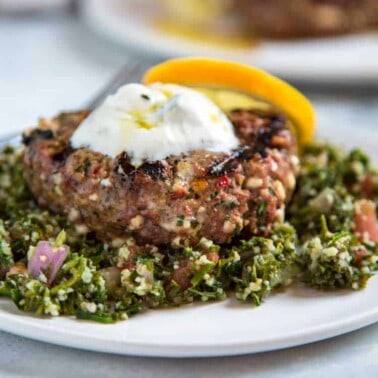 closeup photo of ground lamb burger on plate with fresh herbs