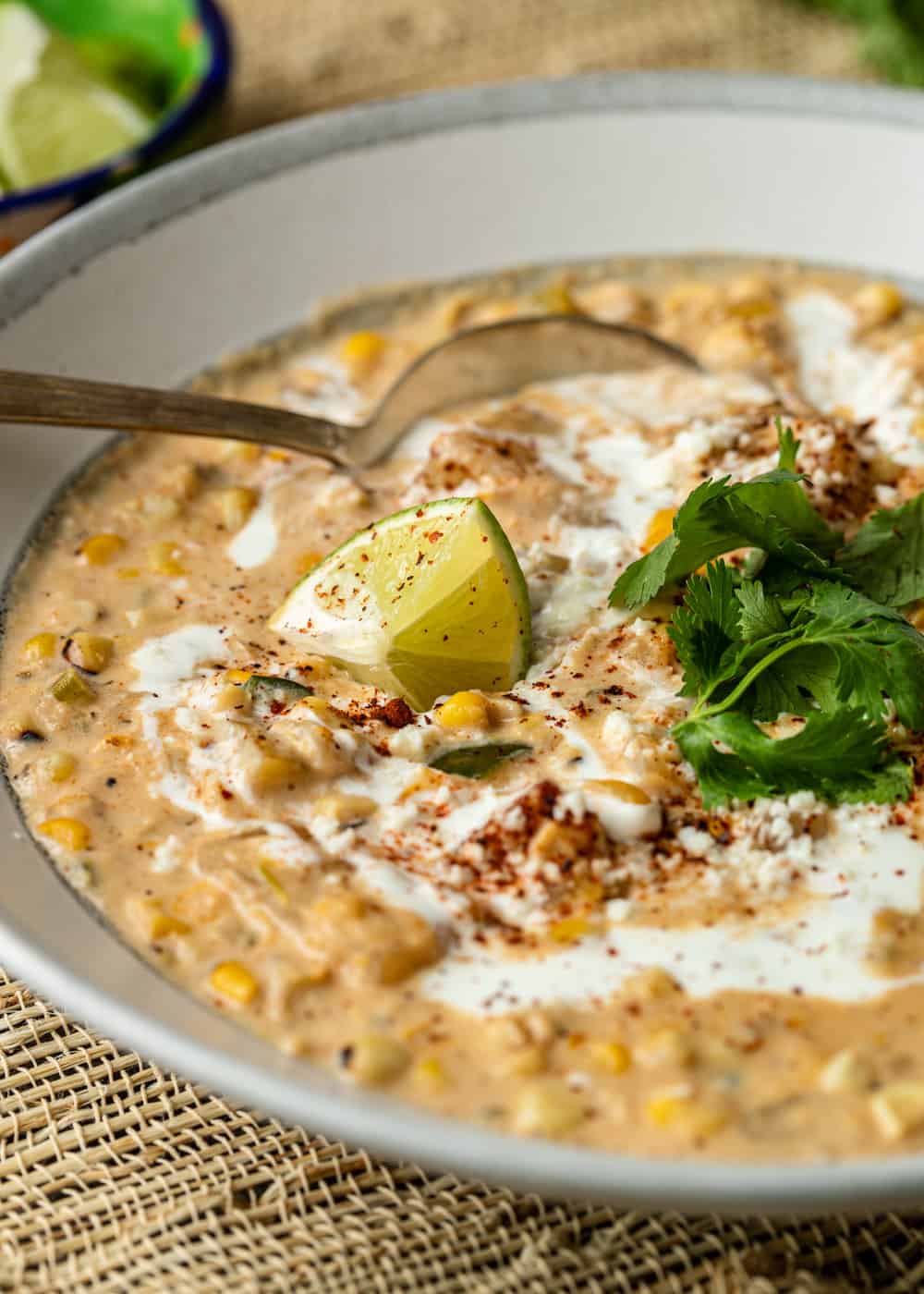 close up of a metal spoon in a bowl of mexican corn chowder topped with fresh cilantro and a lime wedge