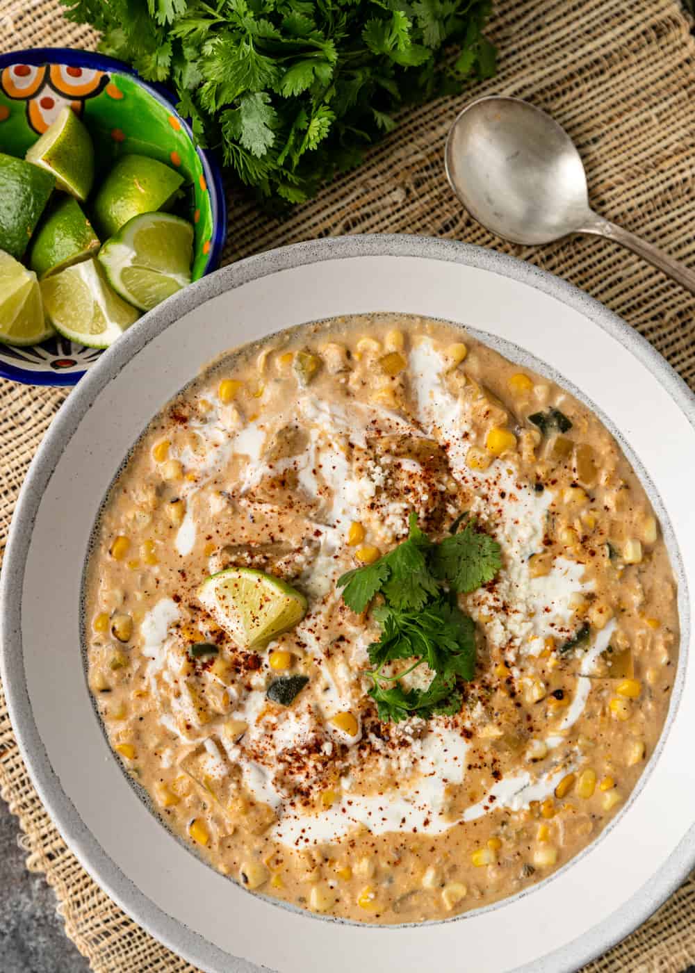 poblano corn chowder in a white bowl next to lime wedges, cilantro, and a spoon