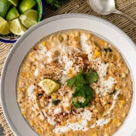 mexican corn chowder in a white bowl next to lime wedges, cilantro, and a spoon