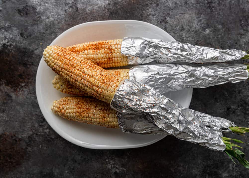 ears of corn wrapped in foil and seasoned for a street corn recipe