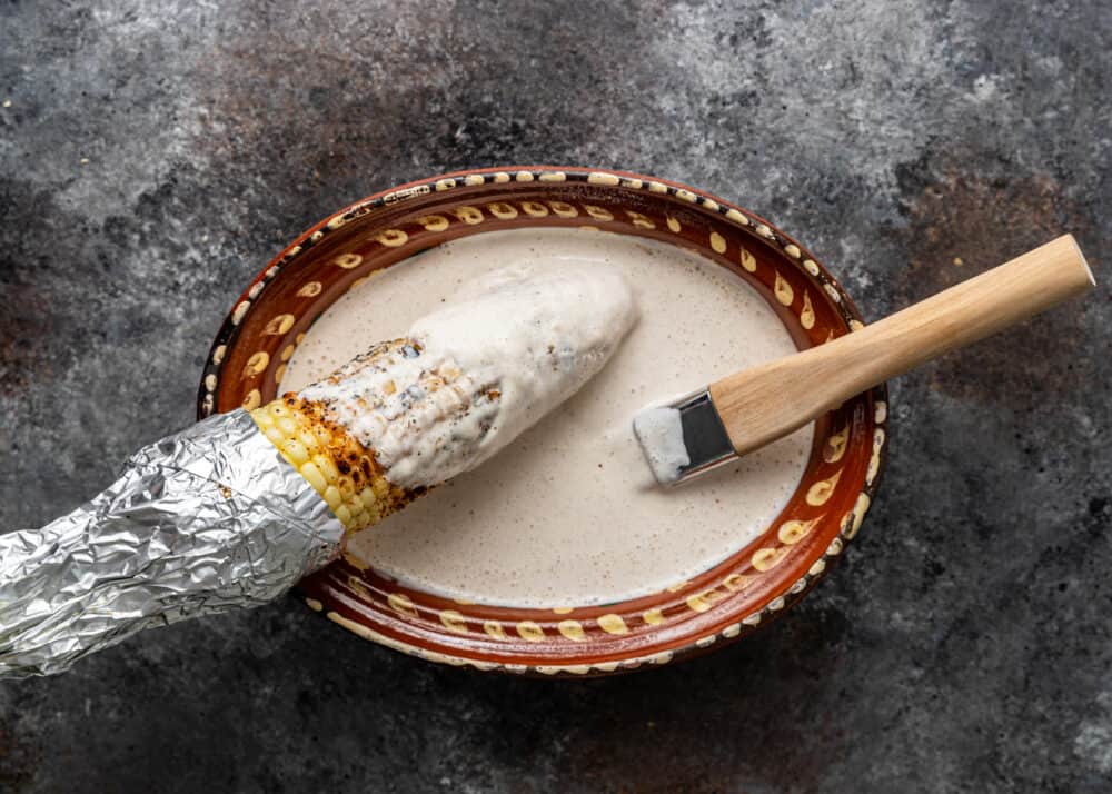 brushing Mexican crema onto roasted corn on the cob