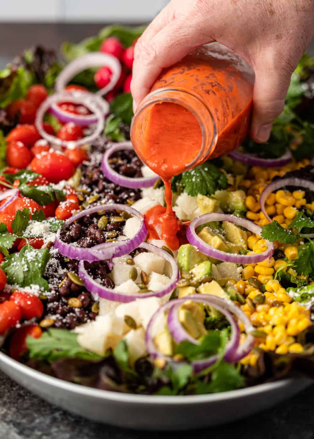 pouring roasted tomato vinaigrette over white bowl of salad