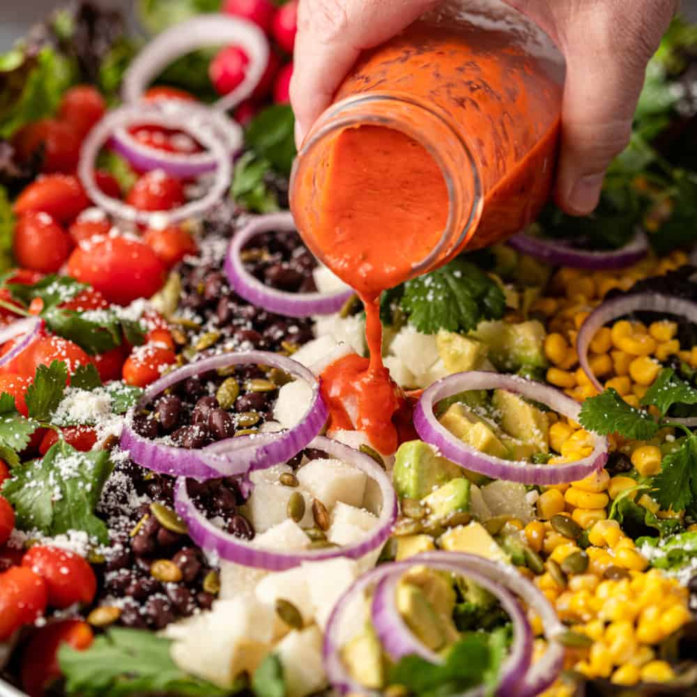 pouring tomato vinaigrette over Mexican salad