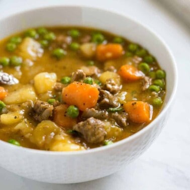 bowl of swiss steak stew made of tender beef in gravy with carrots, peas and potatoes