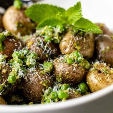 bowl of pesto potato salad garnished with fresh herbs