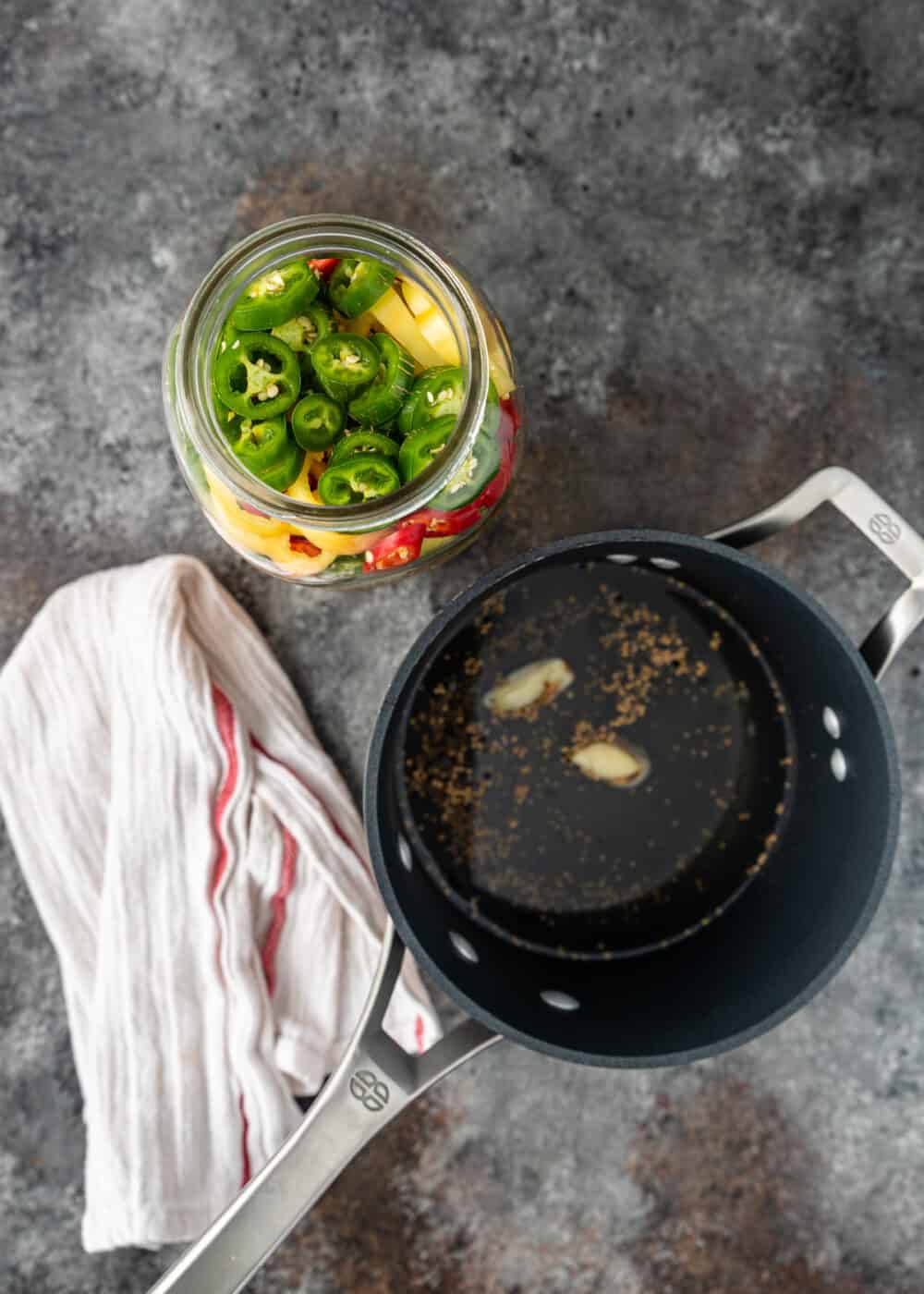 overhead: saucepan of brine for pickled peppers next to jar of jalapeno slices